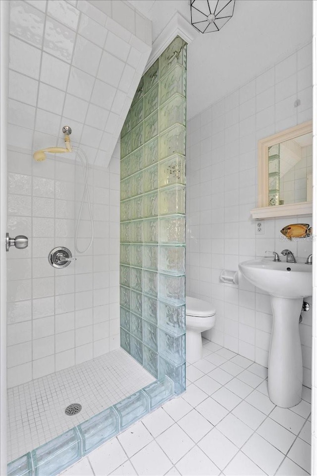 bathroom with tile patterned flooring, a tile shower, toilet, and tile walls