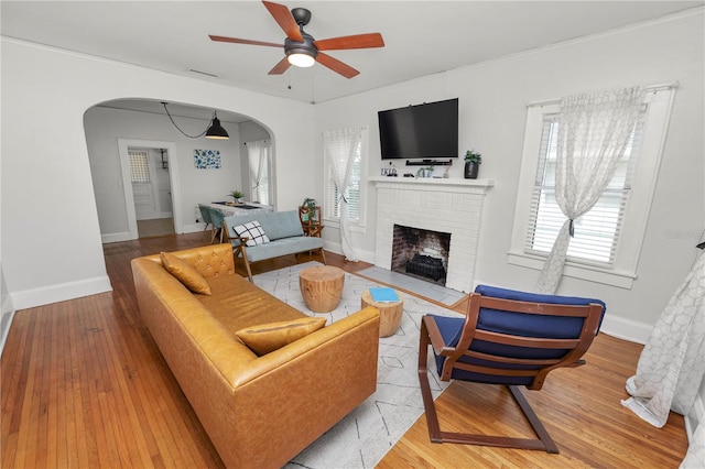 living room with ornamental molding, light hardwood / wood-style flooring, a brick fireplace, and ceiling fan