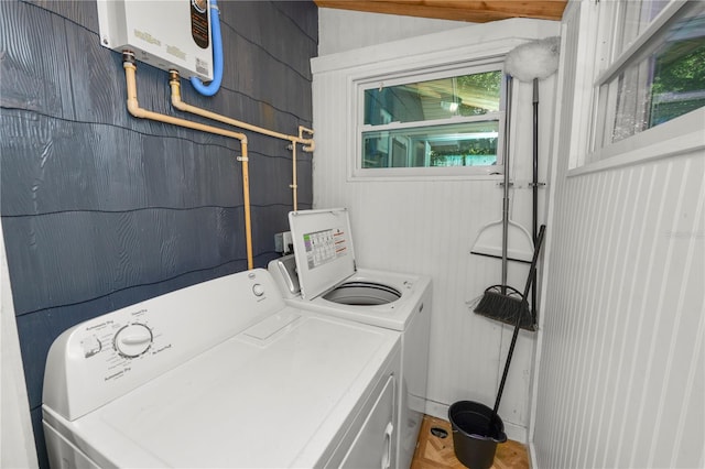 clothes washing area with water heater, washer and dryer, and wooden walls