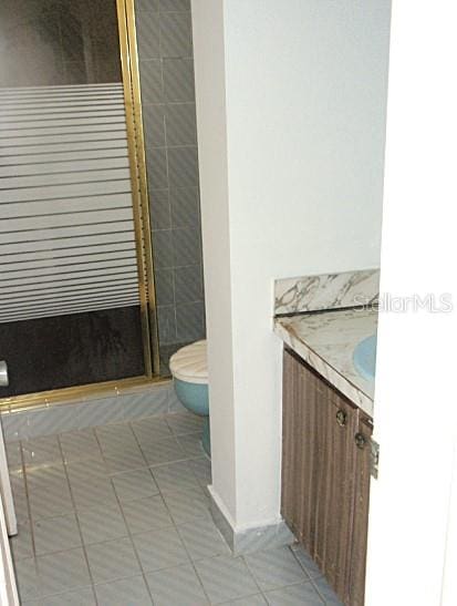 bathroom with toilet, vanity, tile patterned floors, and a shower with shower door