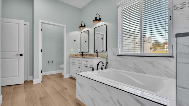 bathroom with a garden tub, toilet, wood finished floors, double vanity, and baseboards