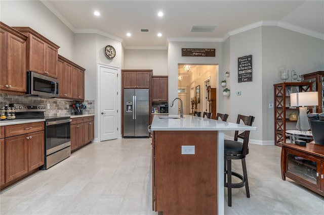 kitchen featuring an island with sink, stainless steel appliances, ornamental molding, sink, and a breakfast bar