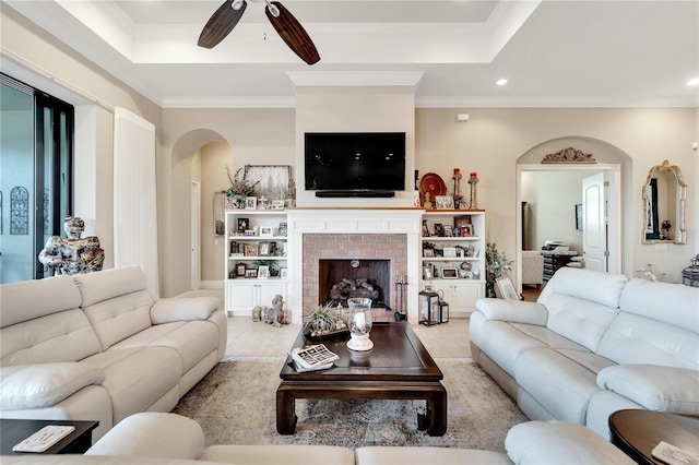 living room featuring crown molding, a tray ceiling, a brick fireplace, and ceiling fan