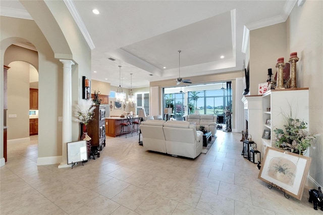 living room with crown molding, a tray ceiling, ceiling fan with notable chandelier, and decorative columns