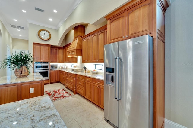 kitchen with crown molding, light tile patterned flooring, stainless steel appliances, custom range hood, and light stone counters