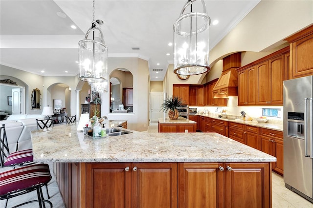 kitchen with hanging light fixtures, light stone counters, a large island with sink, ornamental molding, and stainless steel appliances