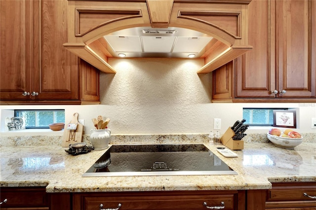 kitchen featuring black electric stovetop, island exhaust hood, and light stone counters