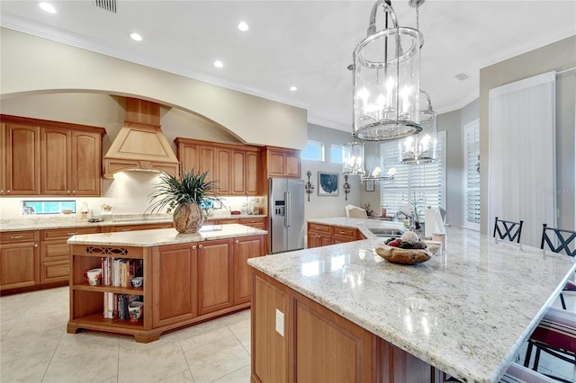 kitchen with a large island, stainless steel fridge with ice dispenser, premium range hood, a kitchen bar, and crown molding