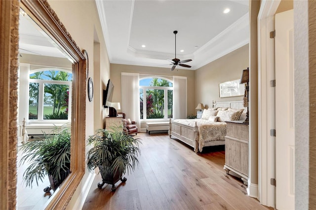 bedroom with ornamental molding, a tray ceiling, light wood-type flooring, and ceiling fan