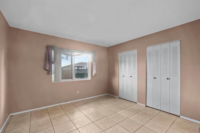 unfurnished bedroom with a textured ceiling, light tile patterned floors, and two closets