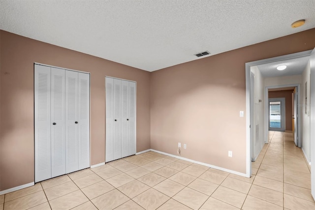 unfurnished bedroom featuring a textured ceiling, two closets, and light tile patterned floors