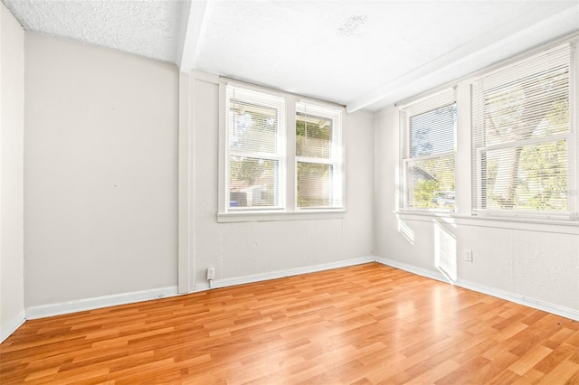 unfurnished room featuring a textured ceiling, beam ceiling, plenty of natural light, and light wood-type flooring