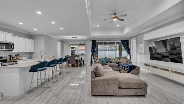 living room with light hardwood / wood-style floors, crown molding, sink, and ceiling fan