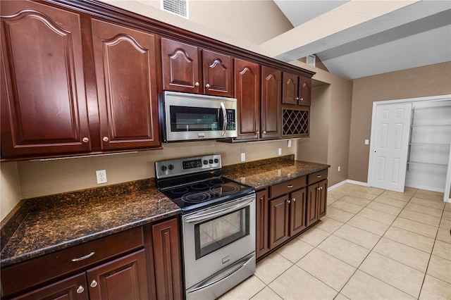 kitchen featuring dark stone countertops, light tile patterned floors, vaulted ceiling, and appliances with stainless steel finishes