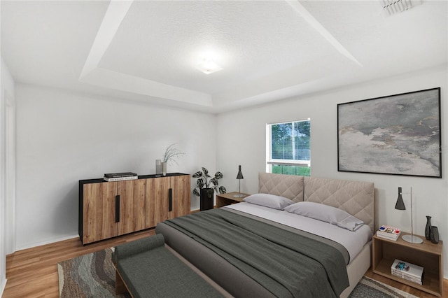 bedroom with a tray ceiling and light hardwood / wood-style floors