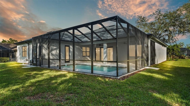 back house at dusk with a patio area, a lanai, and a lawn