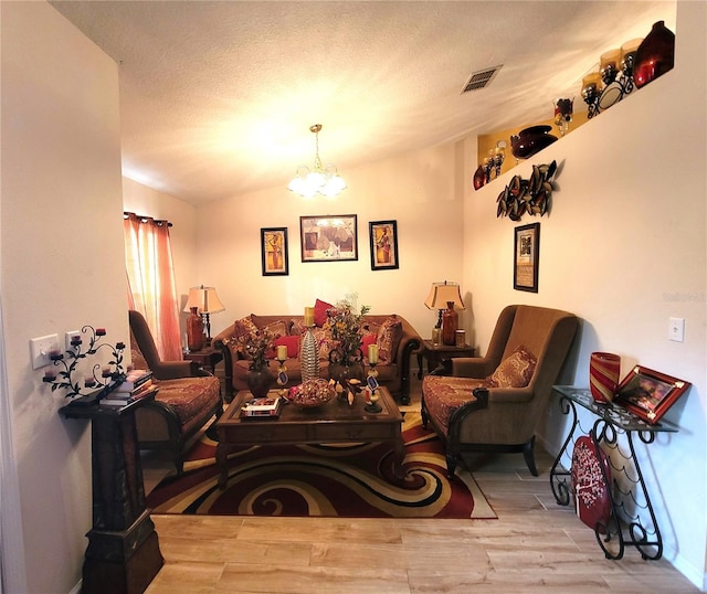 living room with lofted ceiling, a notable chandelier, a textured ceiling, and light wood-type flooring