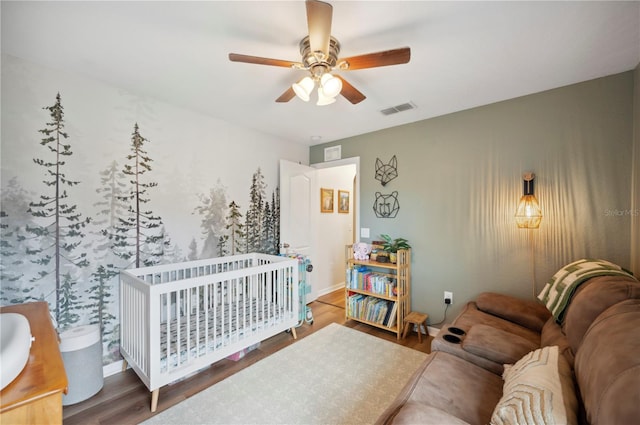 bedroom with hardwood / wood-style flooring, ceiling fan, and a crib