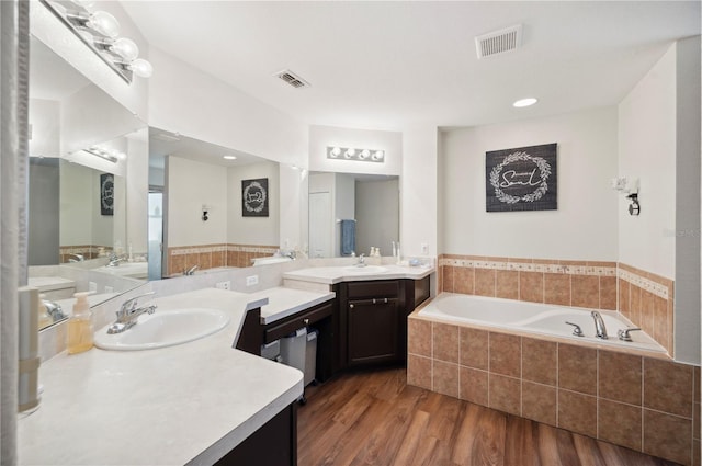 bathroom with hardwood / wood-style floors, vanity, and tiled tub