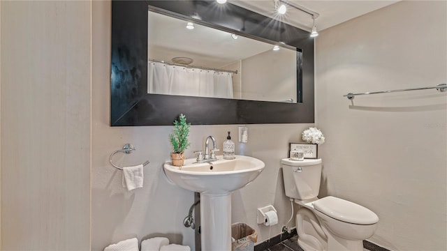 bathroom featuring curtained shower, rail lighting, sink, and toilet