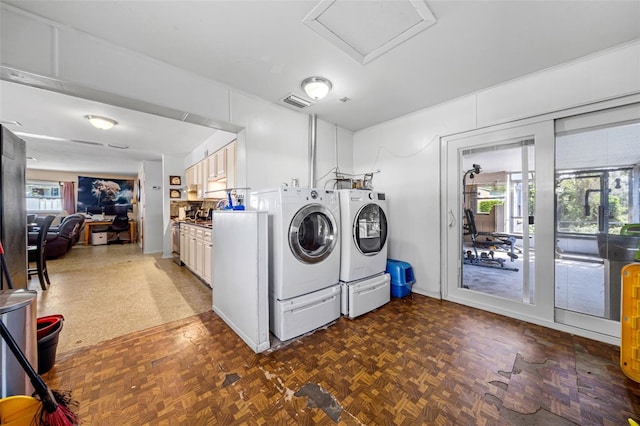 laundry area with dark parquet floors, a healthy amount of sunlight, and washer and clothes dryer