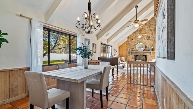 dining area featuring ceiling fan with notable chandelier, high vaulted ceiling, beamed ceiling, a stone fireplace, and wood walls