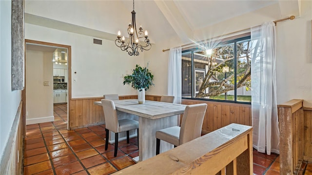 dining room featuring a chandelier, lofted ceiling, and wooden walls