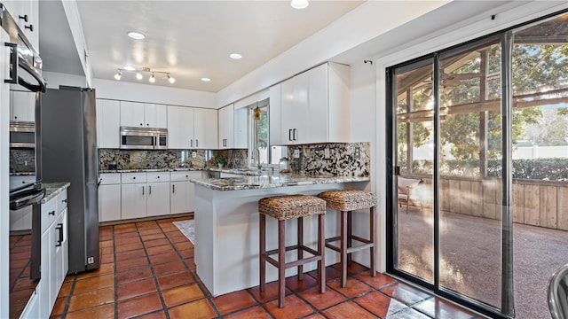 kitchen with white cabinetry, kitchen peninsula, a wealth of natural light, and appliances with stainless steel finishes