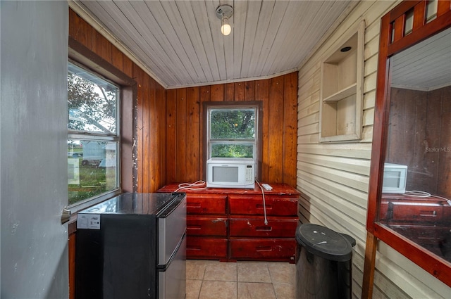 kitchen with a healthy amount of sunlight, wooden walls, light tile patterned floors, and stainless steel refrigerator