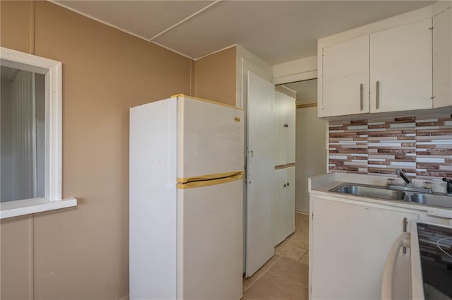 kitchen featuring sink, light tile patterned floors, white cabinetry, decorative backsplash, and white fridge