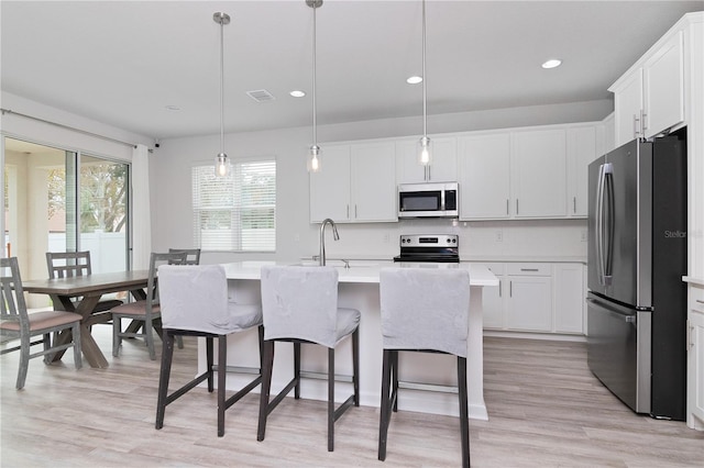 kitchen featuring stainless steel appliances, hanging light fixtures, white cabinets, and a kitchen island with sink