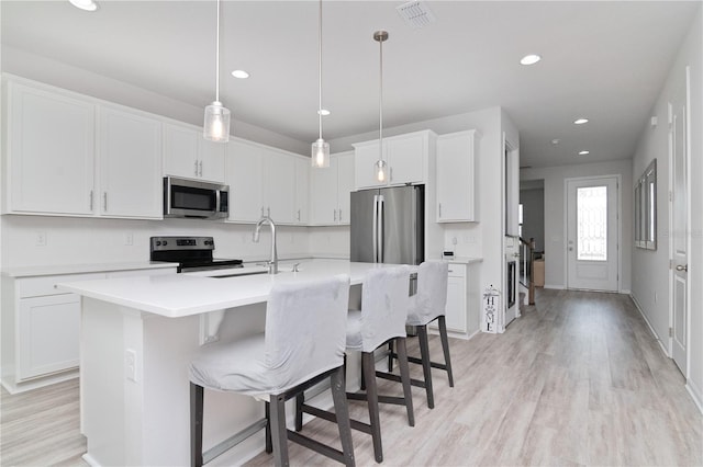 kitchen with light hardwood / wood-style floors, white cabinets, a kitchen island with sink, pendant lighting, and appliances with stainless steel finishes