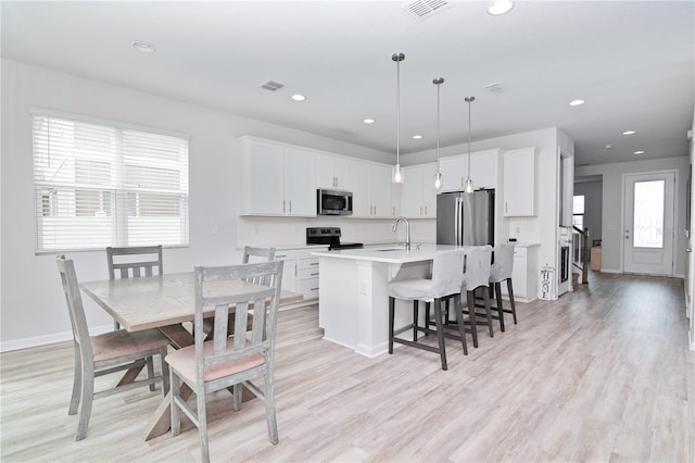 kitchen featuring stainless steel appliances, a center island with sink, sink, decorative light fixtures, and white cabinets