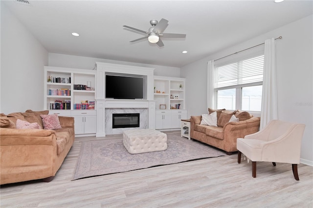 living room with ceiling fan, a high end fireplace, and light hardwood / wood-style floors