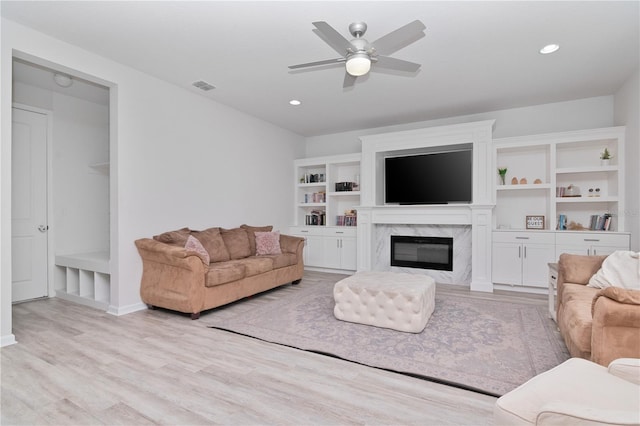 living room featuring light hardwood / wood-style floors, ceiling fan, and a premium fireplace