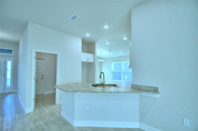 kitchen with a wealth of natural light, kitchen peninsula, sink, and white cabinets