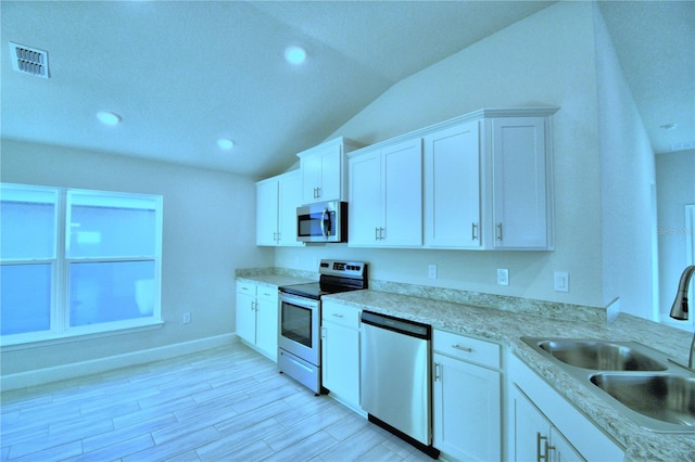 kitchen with stainless steel appliances, lofted ceiling, white cabinets, sink, and light hardwood / wood-style flooring