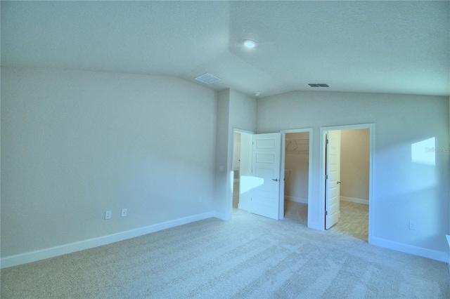 unfurnished bedroom featuring light carpet, a textured ceiling, a walk in closet, a closet, and vaulted ceiling