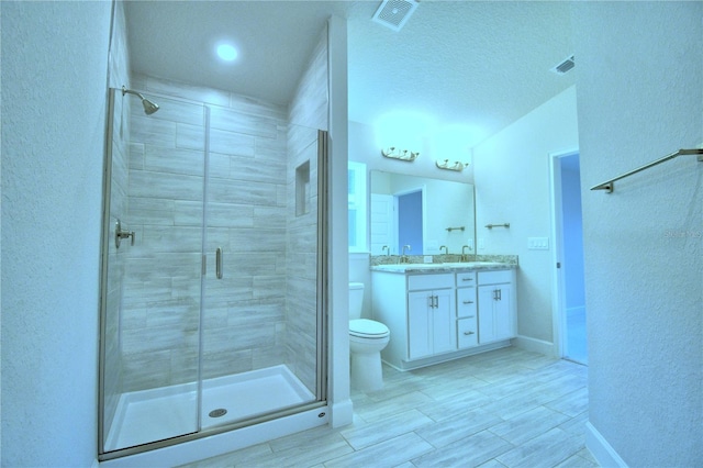 bathroom with a textured ceiling, wood-type flooring, vanity, a shower with shower door, and toilet