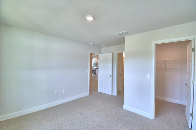 unfurnished bedroom with a closet, a spacious closet, and light carpet