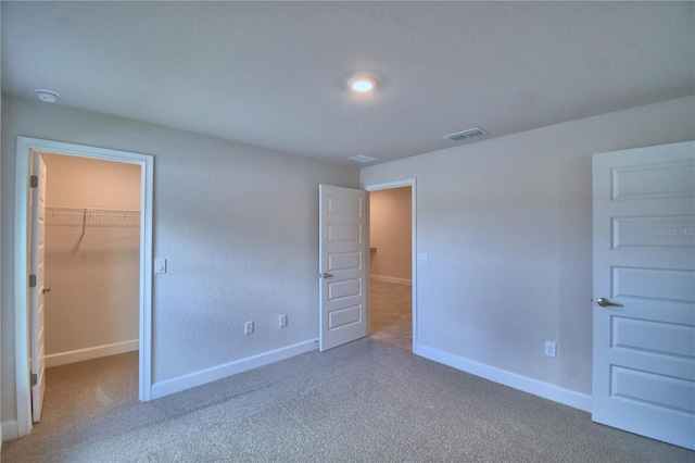 unfurnished bedroom with a closet, a spacious closet, and carpet