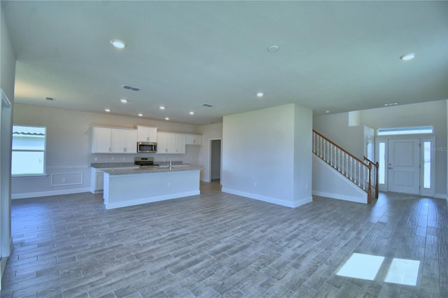 kitchen featuring open floor plan, a center island with sink, appliances with stainless steel finishes, and light wood finished floors