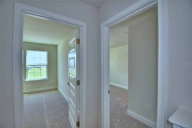 hall with visible vents, baseboards, and carpet flooring