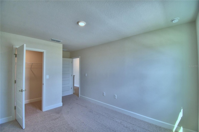 unfurnished bedroom featuring a closet, light colored carpet, a spacious closet, visible vents, and baseboards