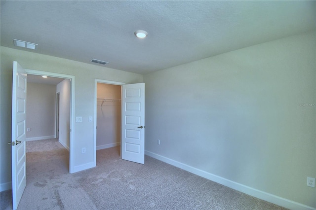 unfurnished bedroom featuring a closet, baseboards, a walk in closet, visible vents, and carpet