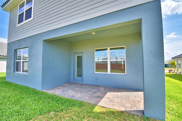 back of house with a patio area, a lawn, and stucco siding