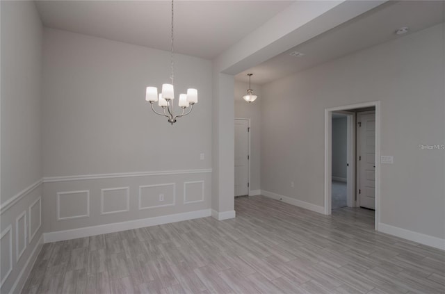 spare room with a chandelier and light wood-type flooring