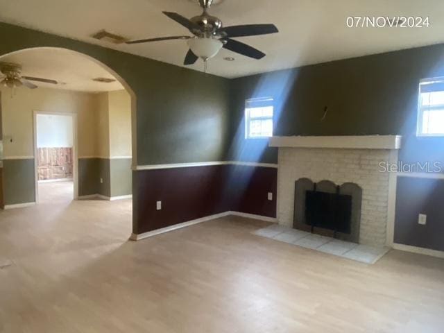 unfurnished living room featuring a fireplace, light wood-type flooring, and ceiling fan