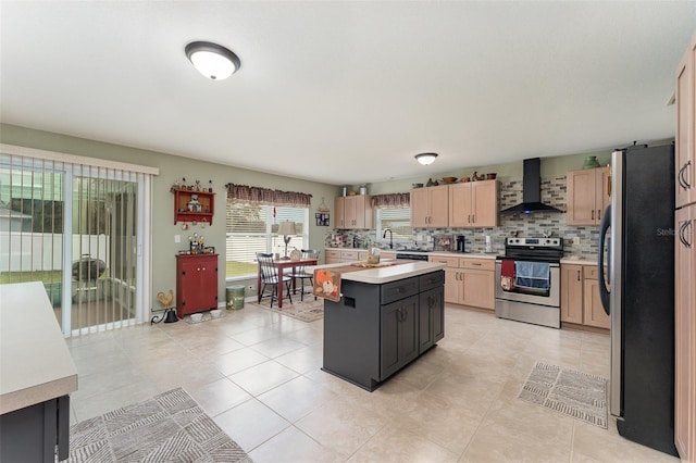 kitchen with sink, a kitchen island with sink, appliances with stainless steel finishes, light brown cabinets, and wall chimney exhaust hood