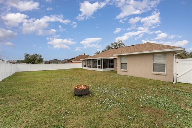 rear view of property with a lawn, a sunroom, and a fire pit